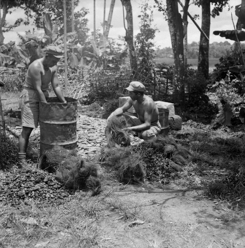 Twee soldaten. Een staat bij een olievat. De ander houdt sisal of vlas vast, Bestanddeelnr 13058