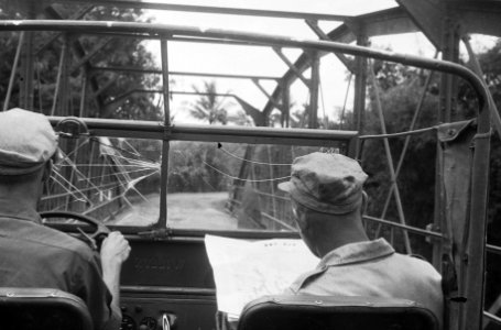 Twee militairen in een jeep rijden over een brug. De rechter bestudeert een kaa, Bestanddeelnr 1561-2-4
