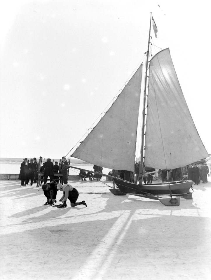 Twee mensen binden hun schaatsen onder bij een ijszeilboot op het ijs van de Go…, Bestanddeelnr 189-1071