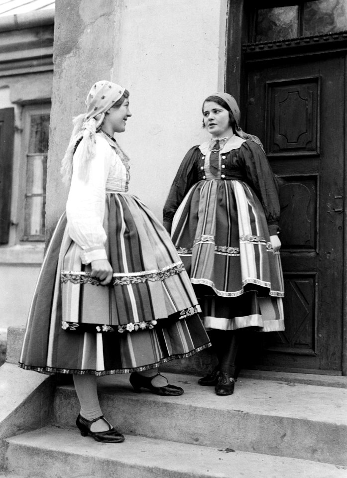 Twee jonge vrouwen in klederdracht op de trap voor hun woning in Lowicz, Bestanddeelnr 252-1289