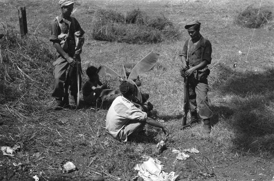Twee KNIL militairen bewaken een zittende Indonesiër. Bij hem zitten twee hele , Bestanddeelnr 20-6-3