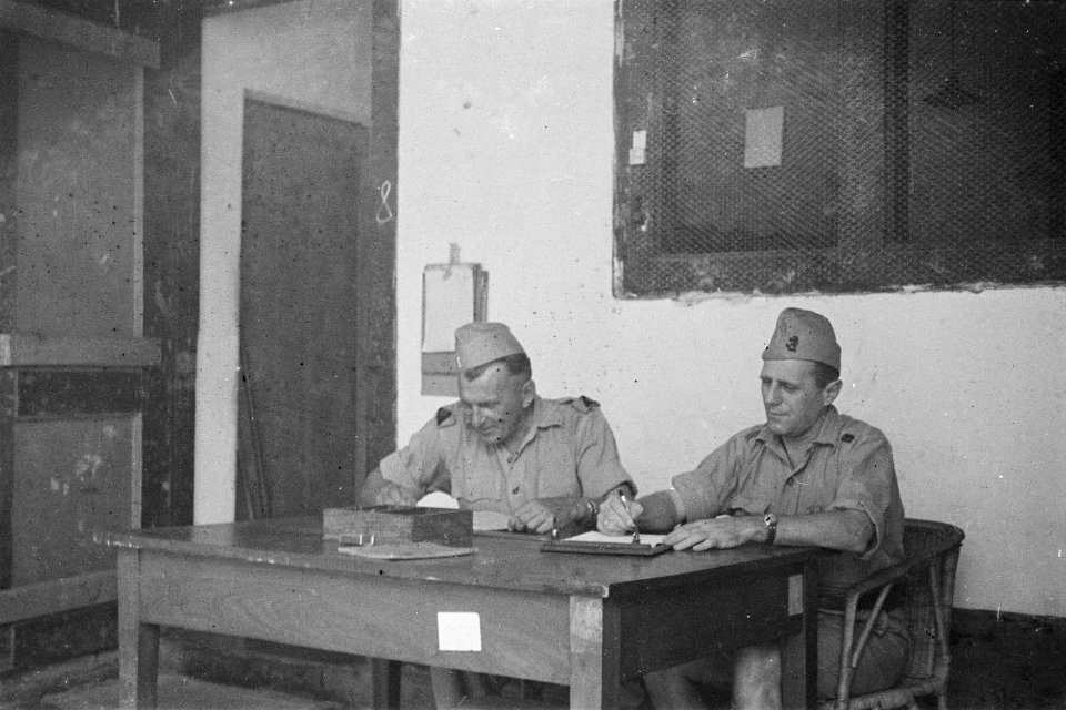 Twee oudere KNIL militairen achter een tafel maken notities, Bestanddeelnr 195-5-2