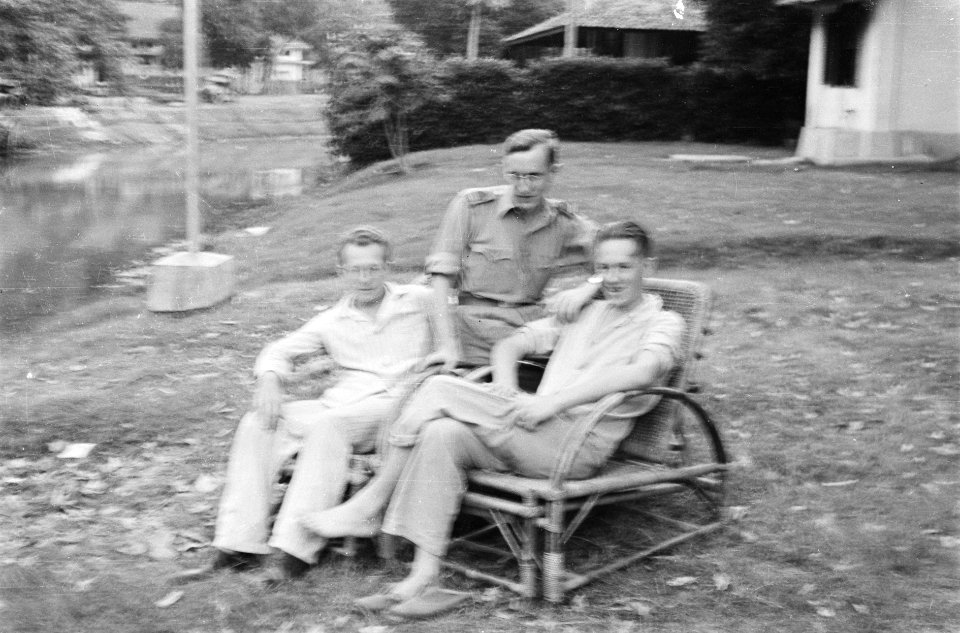 Twee mannen in pyjama zitten in rieten stoelen. Tussen hen een bestuursambtenaar, Bestanddeelnr 208-5-9