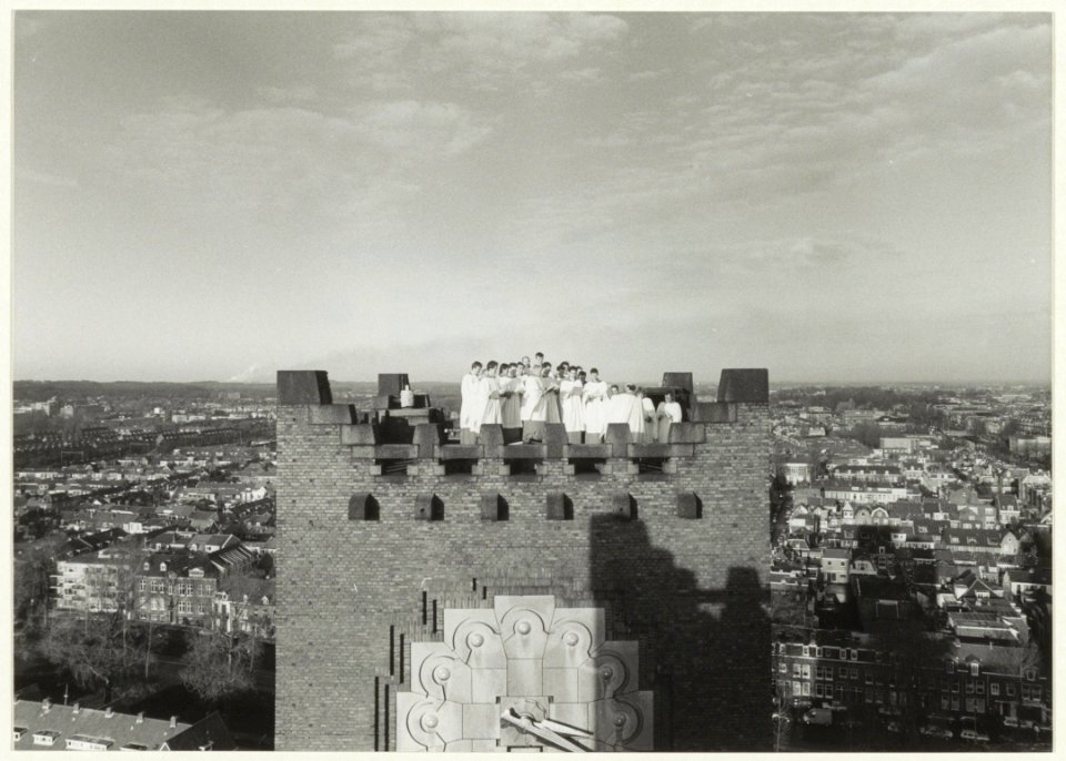 Twintig leden van het Kathedrale Koor van de Bavo zingen bovenop de vrouwentoren, t.g.v. hun 50-jarig jubileum. NL-HlmNHA 54031859
