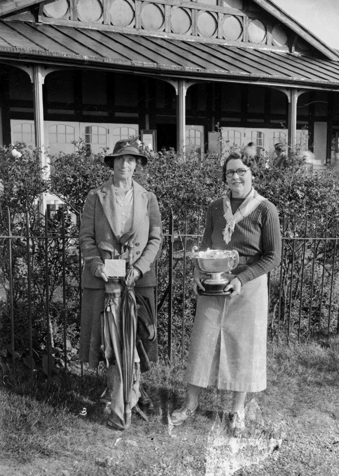 Two lady golfers outside Llandrindod Wells Golf Club pavilion, one holding a cup (1294136)