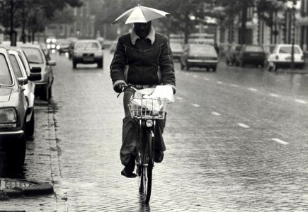 Onder moeders paraplui', Norris Bennet (folk-muziekant) op de fiets. Aangekocht in 1987 van United Fotos de Boer bv. - Negatiefnummer 25593 k 24. - Gepubliceerd in het Haarlems Dagblad van 09.10.1985