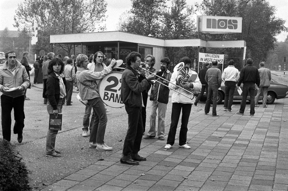 Postende omroepmedewerkers maken muziek voor de toegangspoort van de NOS in Hilv, Bestanddeelnr 931-7434