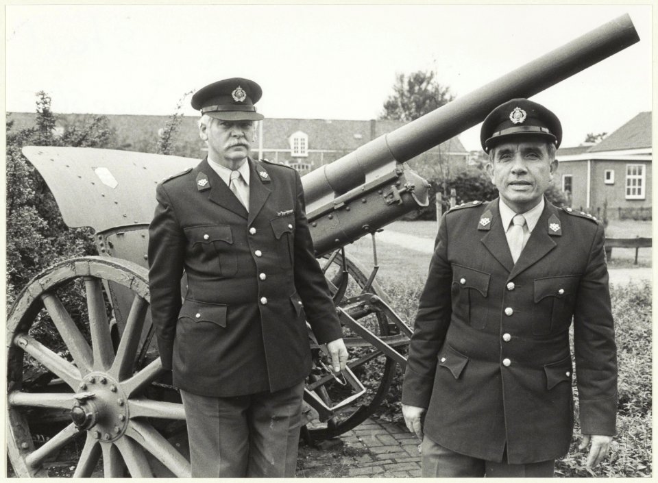 Portret van kapitein P. Schuler, kazernecommandant en een onbekende militair, poserend voor een kanon op het terrein van de Ripperda kazerne. NL-HlmNHA 54026212