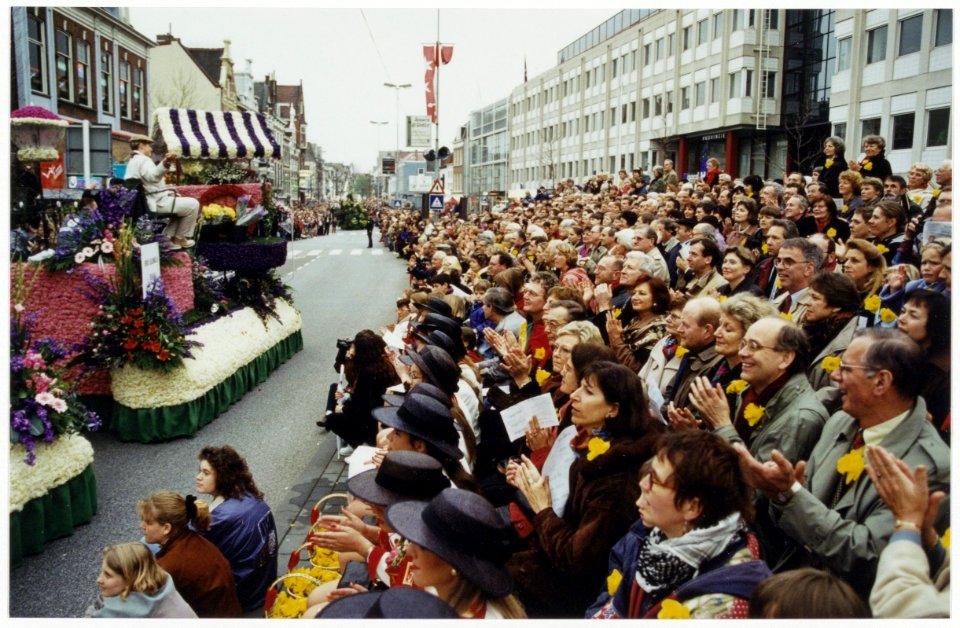 Praalwagens van het bloemencorso trekken voorbij aan de VIP-tribune op het Houtplein. NL-HlmNHA 54036115
