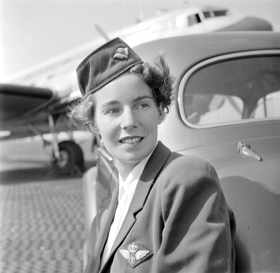 Portret van een KLM stewardess leunend tegen een auto met op de achtergrond een , Bestanddeelnr 255-8963