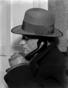 Reiziger met hoed met hoorn van telefoon in gehandschoende hand, Bestanddeelnr 252-1000