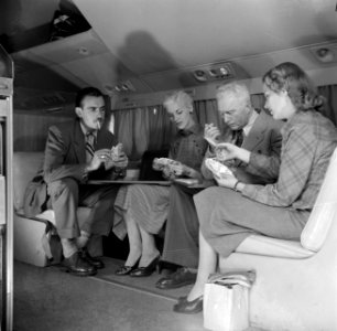Reizigers ontspannen zich aan boord van een KLM passagiersvliegtuig met een kaar, Bestanddeelnr 252-1242