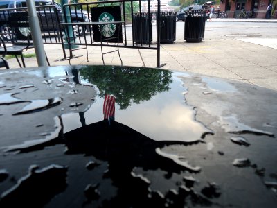 Reflection in water showing a flag on a table outside a Starbucks in Summit NJ