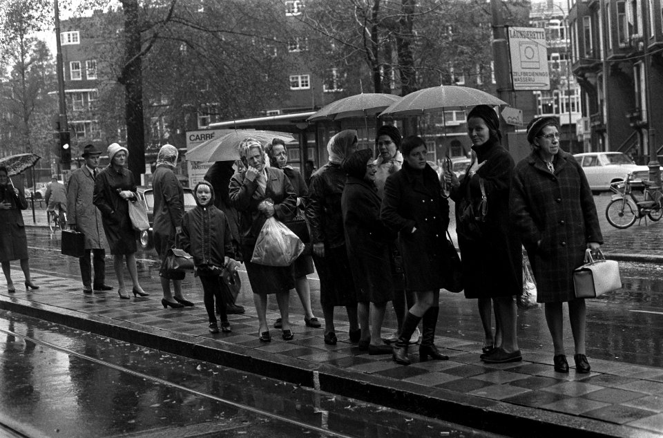 Regen in Amsterdam. Trampassagiers op vluchtheuvel met paraplues, Bestanddeelnr 922-9383