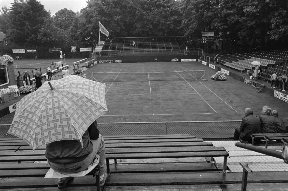 Regen bij tennis op Melkhuisje man met paraplu op tribune, Bestanddeelnr 933-3820