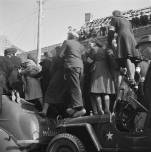 Publiek staat bovenop jeeps en autos of op daken van huizen om een glimp van ko, Bestanddeelnr 900-4021