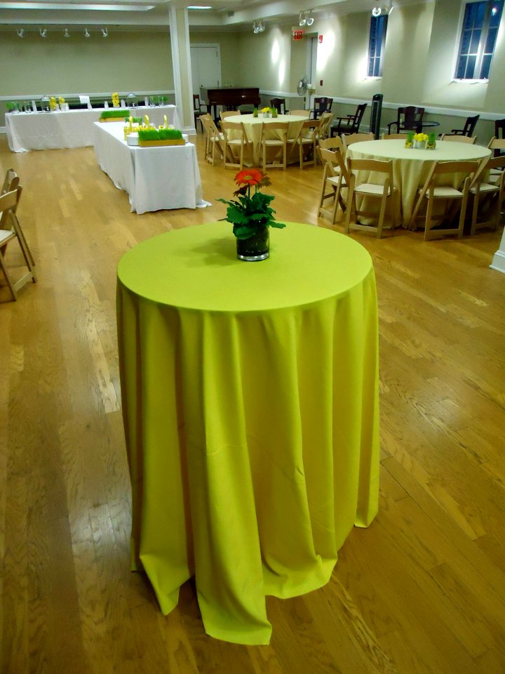 Round high table with a yellow tablecloth with a flower arrangement
