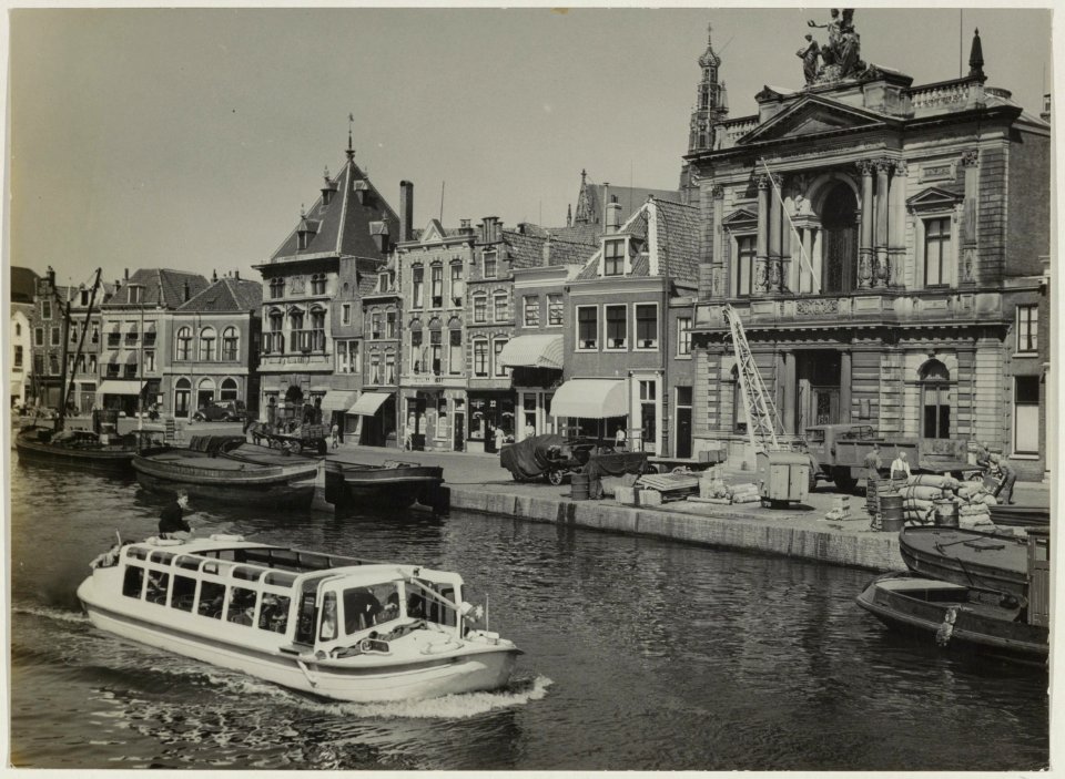 Rondvaartbootje naar Groenendaal vaart over het Spaarne met op de achtergrond de panden van de Korenbeurs en het Teylers Museum