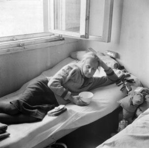 Repatriante ligt op een bed met in haar handen een kom en op bed stukken brood, Bestanddeelnr 900-5088