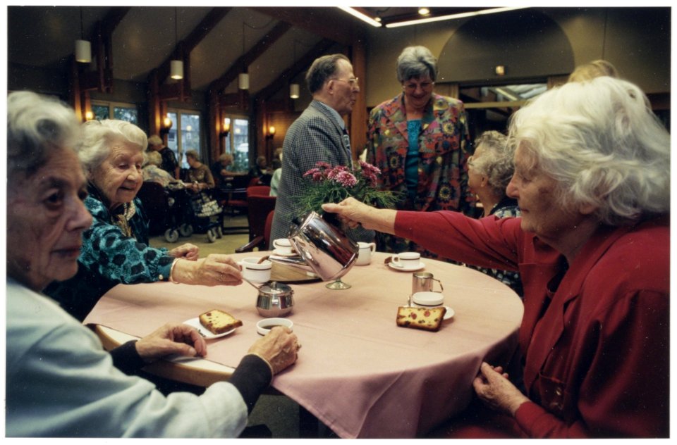 Veertig-jarig bestaan van Zorgcentrum de Blinkert. Enkele bewoners aan de koffie met cake in de recreatiezaal. In het midden staand directrice, mevr. van Gendt. NL-HlmNHA 54036443