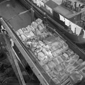 Uitladen van jutezakken uit een binnenvaartschip in de haven van Amsterdam wasg, Bestanddeelnr 255-9462
