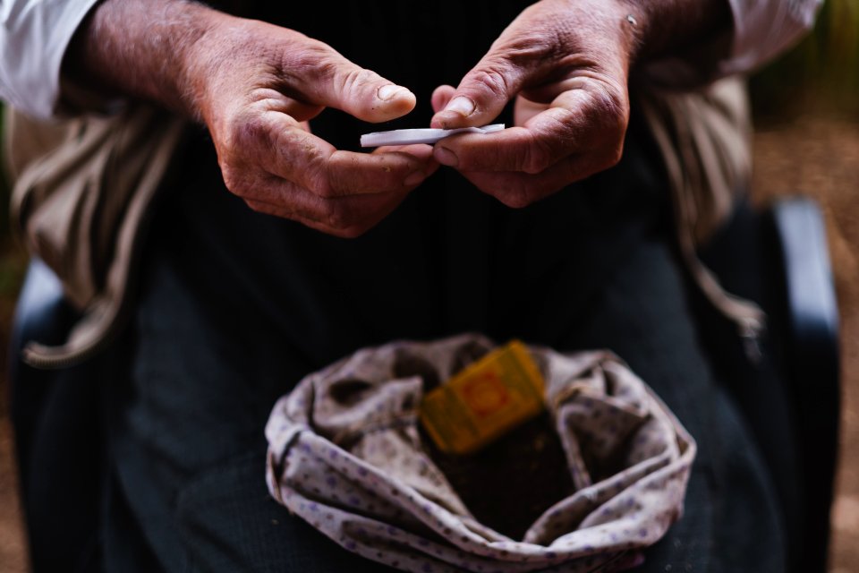 Views in June of 2019 of an Ezidi man in Sardashte Camp for displaced Ezidis rolling a cigarette with tobacco grown nearby atop Shingal mountain 33