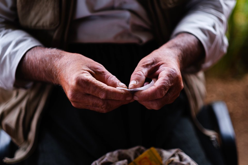 Views in June of 2019 of an Ezidi man in Sardashte Camp for displaced Ezidis rolling a cigarette with tobacco grown nearby atop Shingal mountain 30