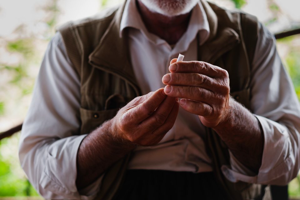 Views in June of 2019 of an Ezidi man in Sardashte Camp for displaced Ezidis rolling a cigarette with tobacco grown nearby atop Shingal mountain 22
