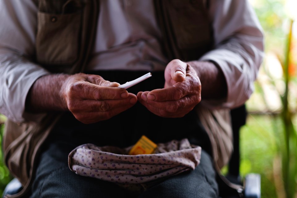 Views in June of 2019 of an Ezidi man in Sardashte Camp for displaced Ezidis rolling a cigarette with tobacco grown nearby atop Shingal mountain 20