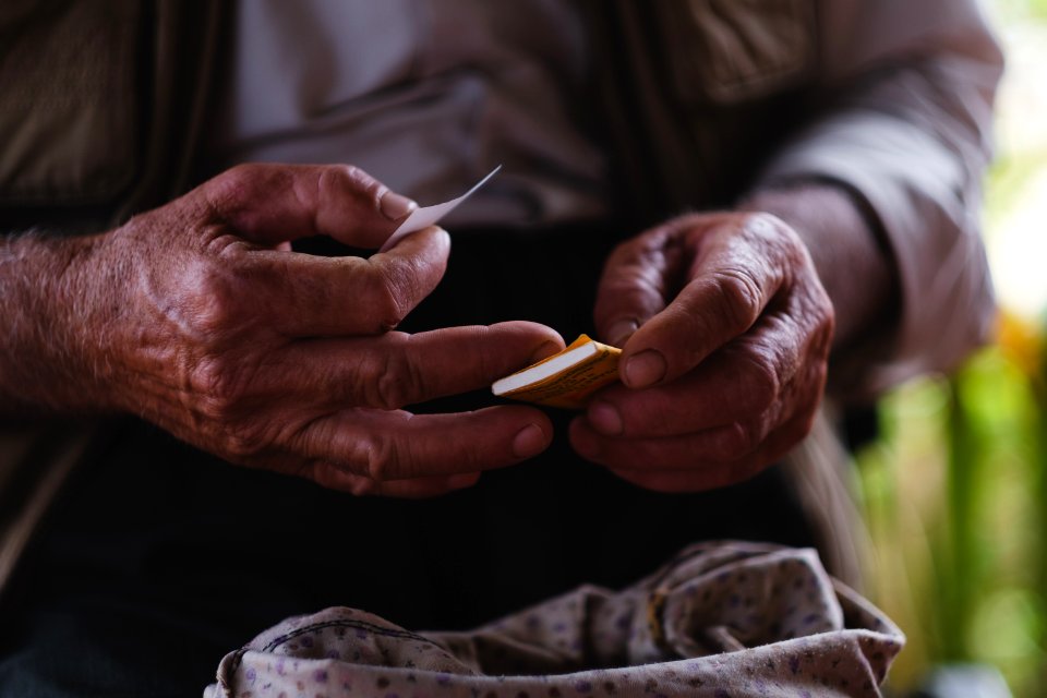 Views in June of 2019 of an Ezidi man in Sardashte Camp for displaced Ezidis rolling a cigarette with tobacco grown nearby atop Shingal mountain 02