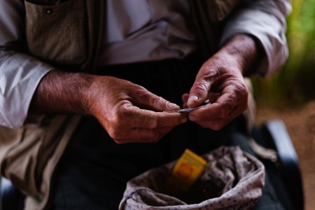 Views in June of 2019 of an Ezidi man in Sardashte Camp for displaced Ezidis rolling a cigarette with tobacco grown nearby atop Shingal mountain 14