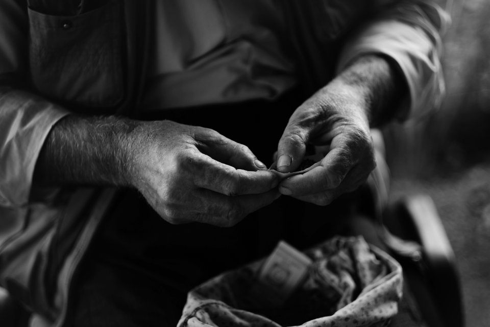 Views in June of 2019 of an Ezidi man in Sardashte Camp for displaced Ezidis rolling a cigarette with tobacco grown nearby atop Shingal mountain 11