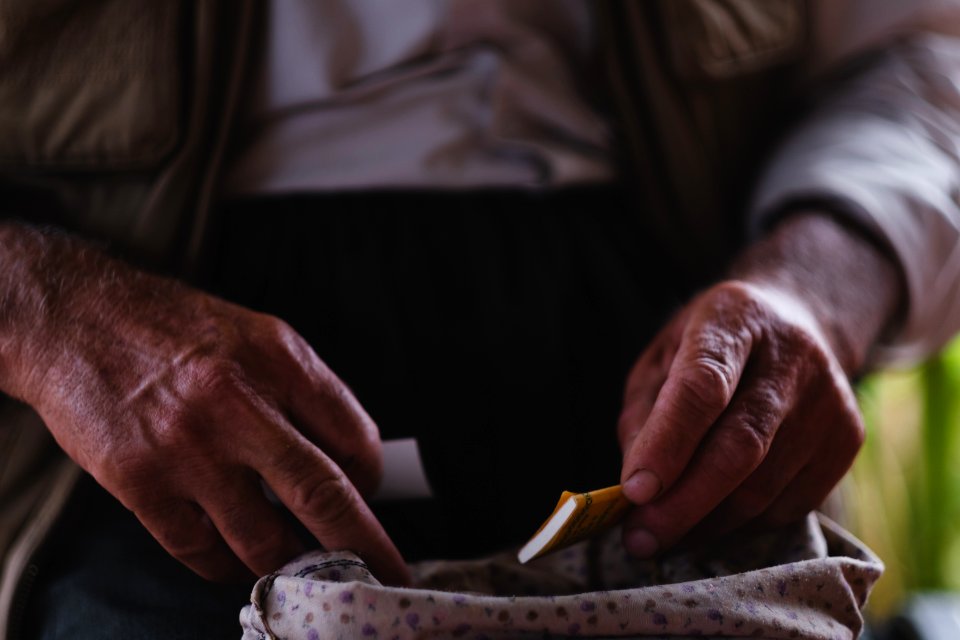 Views in June of 2019 of an Ezidi man in Sardashte Camp for displaced Ezidis rolling a cigarette with tobacco grown nearby atop Shingal mountain 03