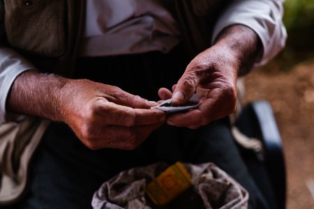 Views in June of 2019 of an Ezidi man in Sardashte Camp for displaced Ezidis rolling a cigarette with tobacco grown nearby atop Shingal mountain 29