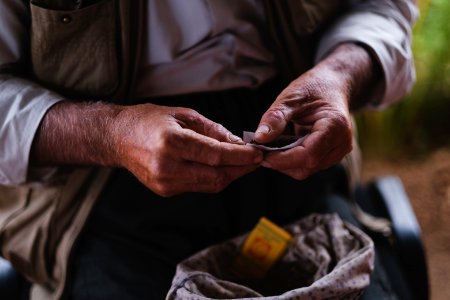 Views in June of 2019 of an Ezidi man in Sardashte Camp for displaced Ezidis rolling a cigarette with tobacco grown nearby atop Shingal mountain 10