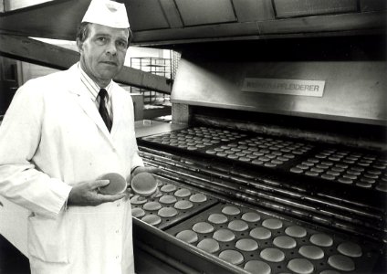 Vermaat-directeur Hennie Budding keurt enkele hamburgerbroodjes die ononderbroken uit de oven schieten, tachtig miljoen per jaar. Aangekocht van United Photos de Boer bv. - Negatiefnummer 38514 k 16. 