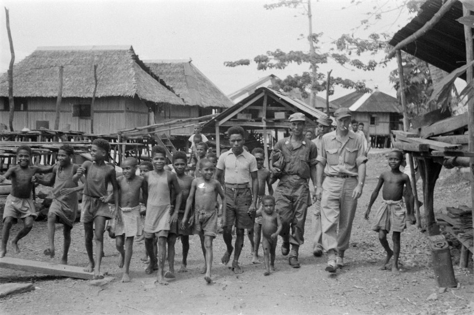 Verslaggever loop met twee KNIL-militairen en een groep kinderen in een Papoea-, Bestanddeelnr 440-6-2