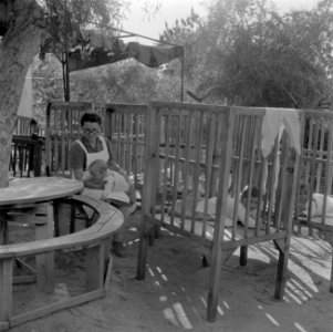 Verzorgster en baby's in boxen bij de kinderopvang van kibboets Kiwath Brenner, Bestanddeelnr 255-0569 photo