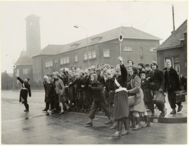 Verkeersbrigadiers met z.g. Endlich-arm, brengen schoolgaande kinderen veilig over de gevaarlijke Rijksstraatweg nabij de Vergierdeweg. NL-HlmNHA 54004512