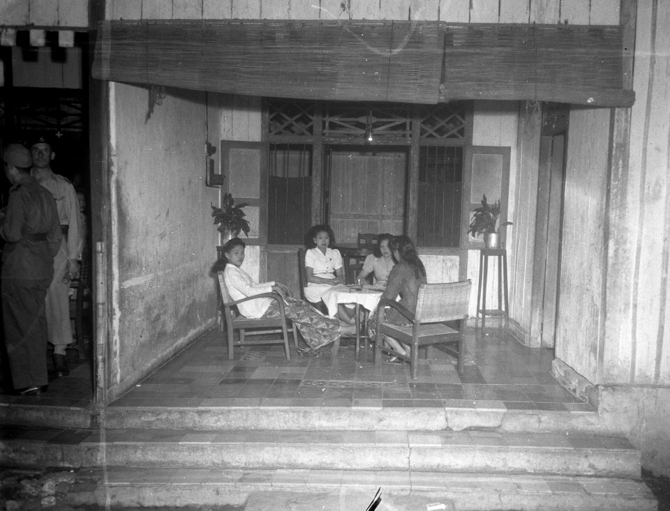 Vier jonge vrouwen (prostituées) zitten op een veranda van een huis. Links mil, Bestanddeelnr 13842
