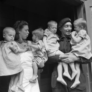 Vier peuters op de armen van een verzorgster en een geuniformeerde man, Bestanddeelnr 900-4880
