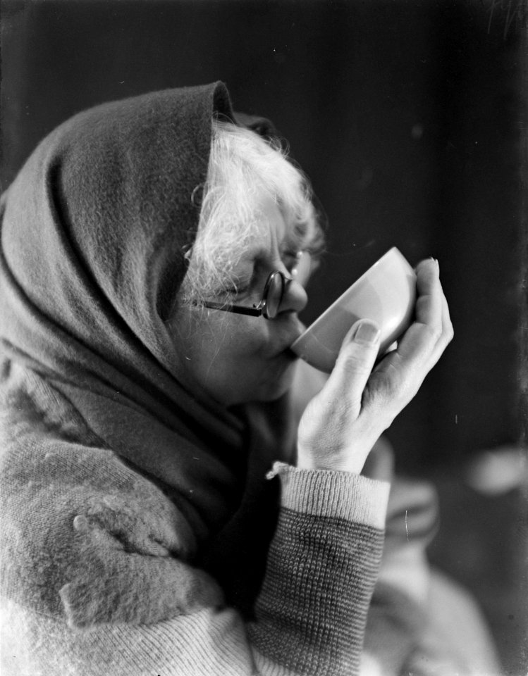 Vrouw met een doek of sjaal om het hoofd geslagen, drinkt een kop koffie, Bestanddeelnr 252-0438