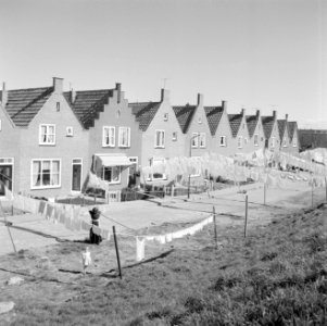 Vrouw in Volendam hangt de was op voor een rij huizen, Bestanddeelnr 254-3835