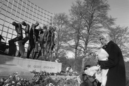 Vrouw met bloemen in de hand staat voor het monument, Bestanddeelnr 934-3873
