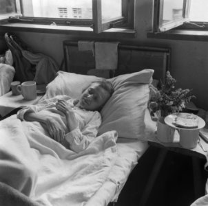 Vrouw ligt op bed met naast haar drinkbekers en een bord met brood, Bestanddeelnr 900-5114