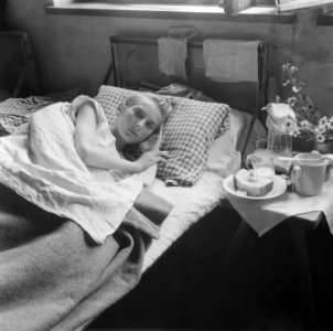 Vrouw ligt op bed met naast haar drinkbekers en een bord met brood, Bestanddeelnr 900-5115