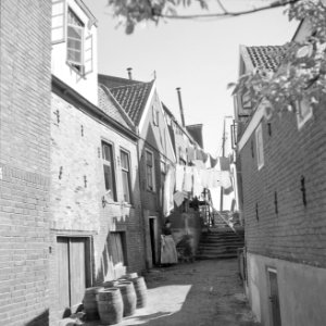 Vrouw in klederdracht bij de was die op straat hangt op de voorgrond staan hout, Bestanddeelnr 254-3985