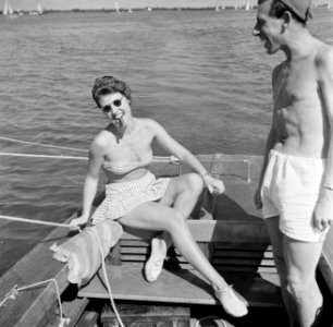 Vrouw in bikini met sigaar in de mond, zittend aan het roer naast staande man, Bestanddeelnr 254-2430