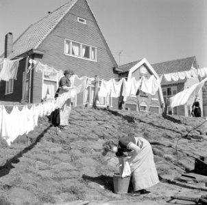 Vrouw in klederdracht is in Volendam bezig met de was die op straat hangt te dro, Bestanddeelnr 254-3840