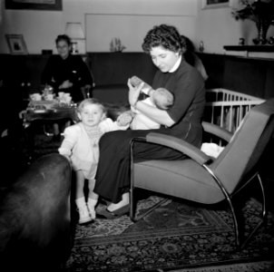 Vrouw houdt een peuter bij de hand terwijl ze een baby de fles geeft, Bestanddeelnr 252-9367